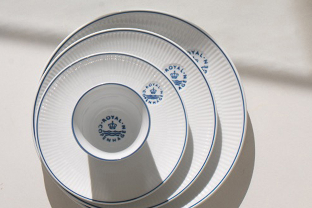 Blueline plates stacked so you can see the fine blue line on all of them. The Blueline Thermal mug stands on top of the stack